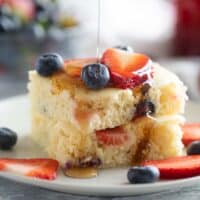 Sheet pan pancakes stacked on a plate with syrup being drizzled over the top.