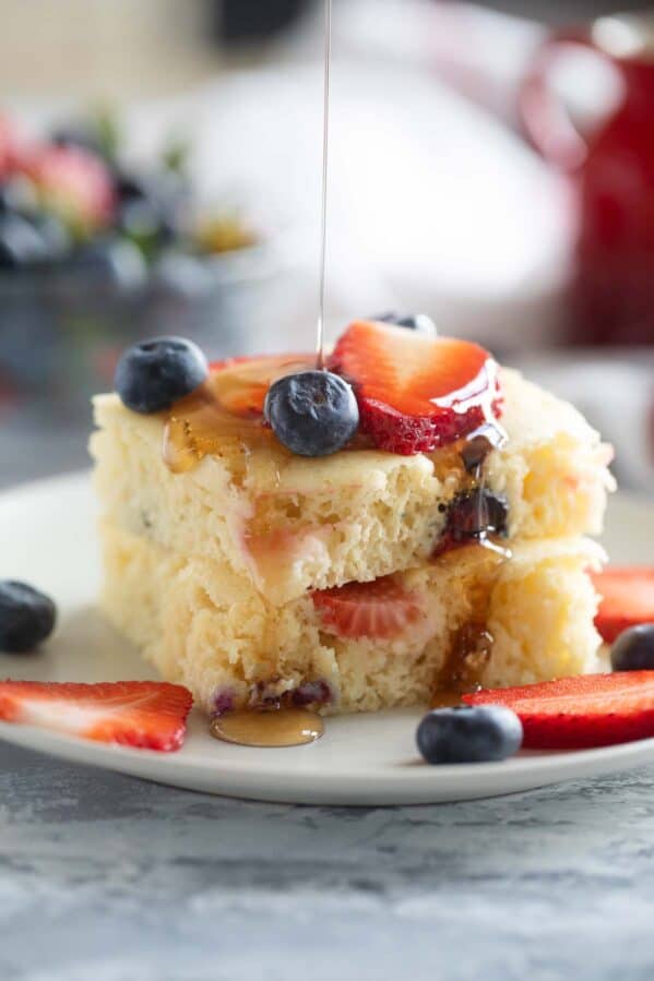 Sheet pan pancakes stacked on a plate with syrup being drizzled over the top.