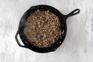 Ground beef and onions cooked in a cast iron skillet.