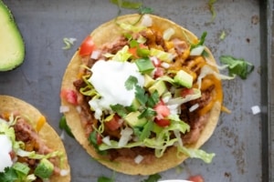 Beef Tostadas topped with lettuce, tomatoes, sour cream, and cilantro.
