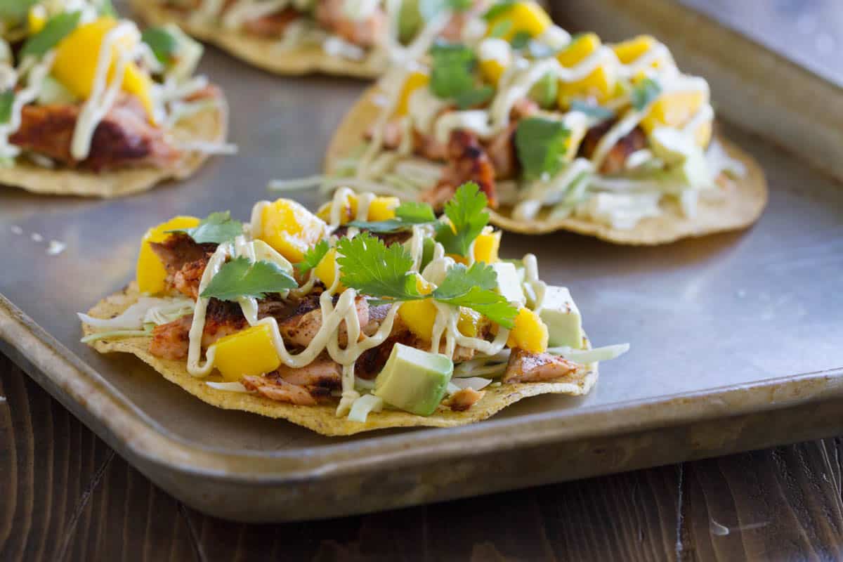 Blackened Salmon Tostadas topped with a creamy sauce, mango, avocado, and cilantro.