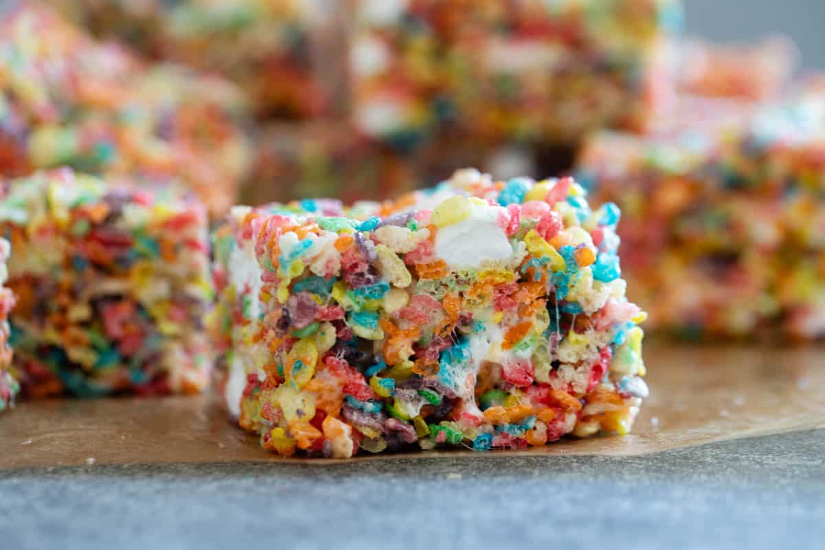 Fruity Pebble Rice Crispy Treats cut into squares on parchment.