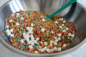 Mixing together fruity pebbles, Rice Krispies, and mini marshmallows.