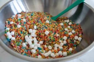 Mixing together fruity pebbles, Rice Krispies, and mini marshmallows.