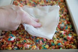 Pressing cereal treats into pan with wax paper.