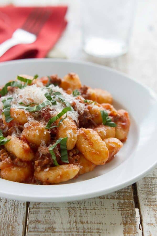 Easy gnocchi with meat sauce, topped with fresh parmesan and fresh basil in a bowl.