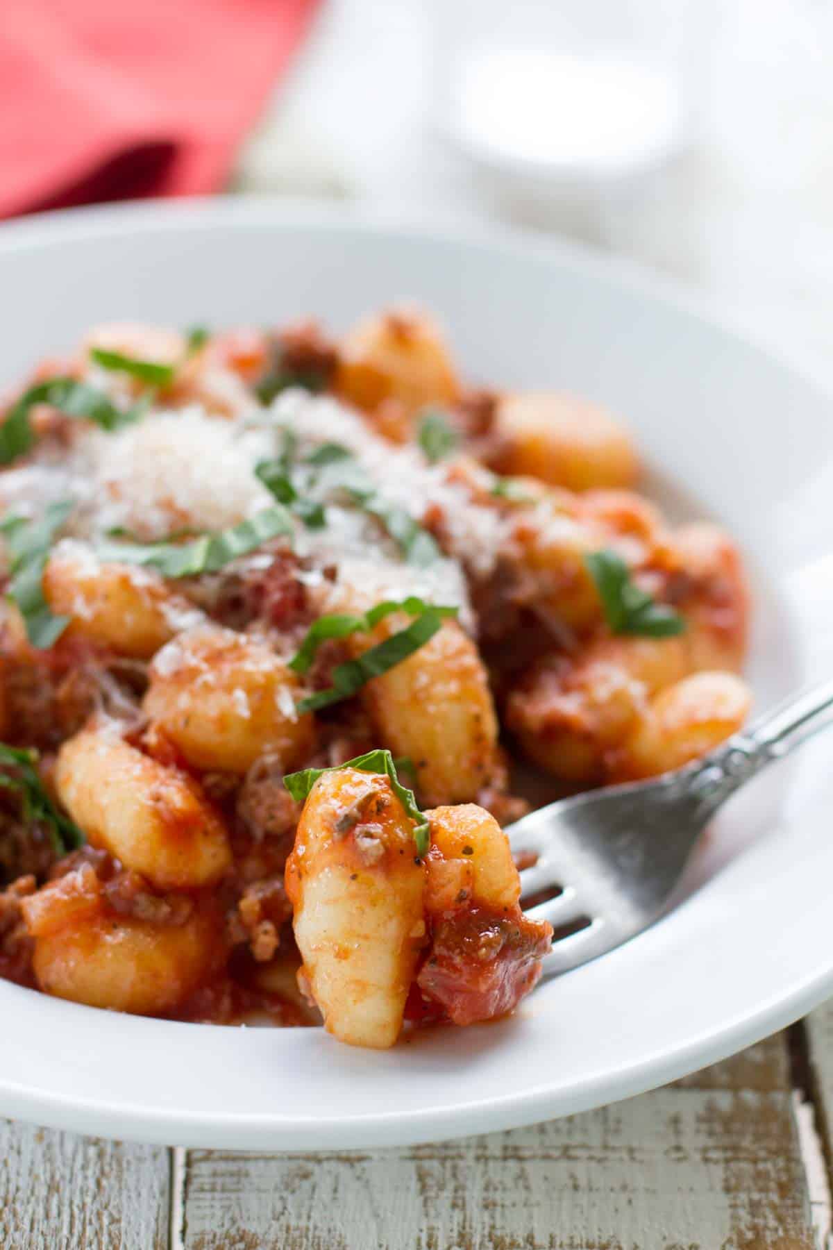 Bowl filled with gnocchi with meat sauce with a gnocchi on a fork.