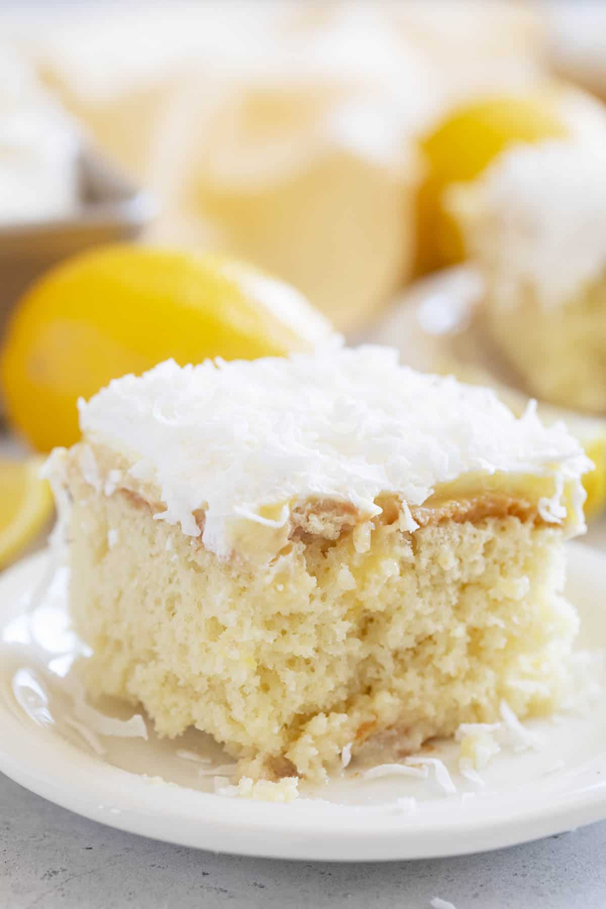 Slice of Lemon Poke Cake with Coconut on a white plate.