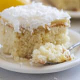 Slice of lemon poke cake with coconut on a plate with a forkful of cake the side.