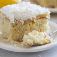 Slice of lemon poke cake with coconut on a plate with a forkful of cake the side.