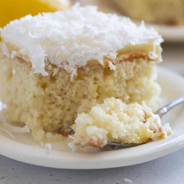 Slice of lemon poke cake with coconut on a plate with a forkful of cake the side.