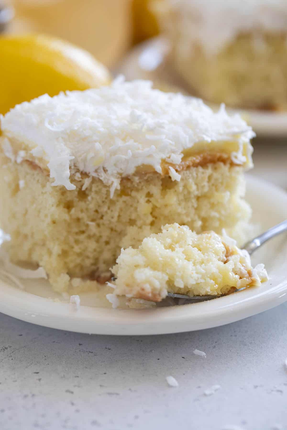 Slice of lemon poke cake with coconut on a plate with a forkful of cake the side.