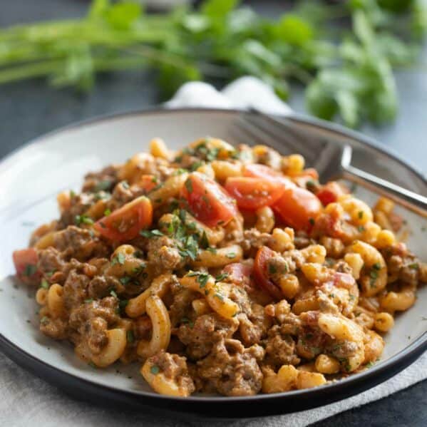 Plate filled with taco Mac and cheese topped with tomatoes and cilantro.