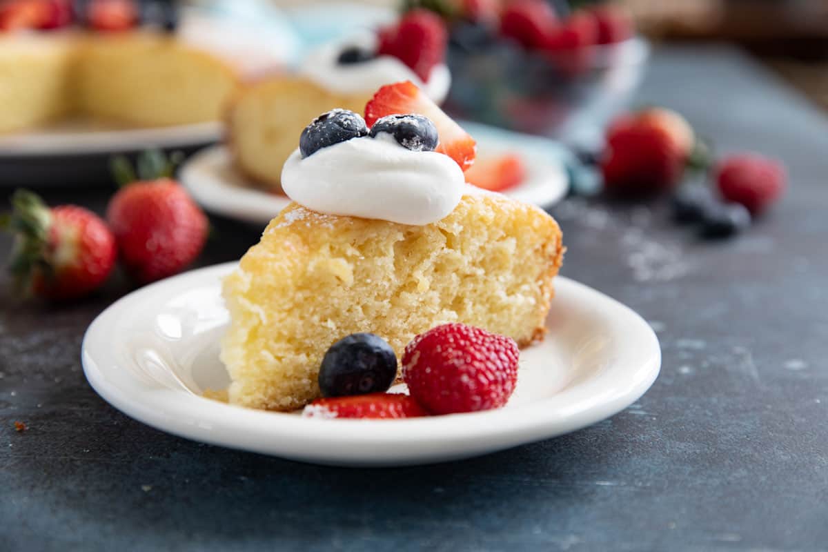 Slice of Yogurt Cake sprinkled with powdered sugar and topped with whipped cream, blueberries, strawberries, and raspberries.