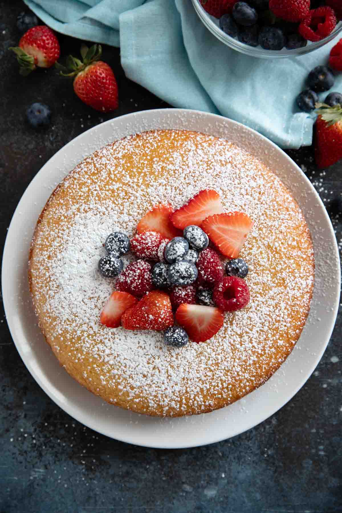 Lemon yogurt cake on a plate, sprinkled with powdered sugar and topped with berries.