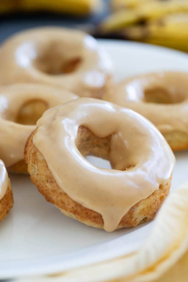 Baked banana donuts on a white plate, frosted with peanut butter icing.