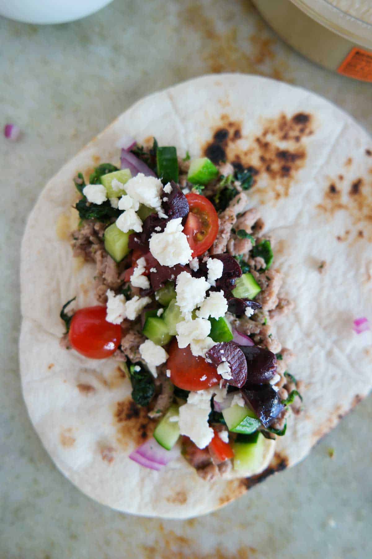 Greek taco on a flour tortilla, topped with olives and feta cheese.
