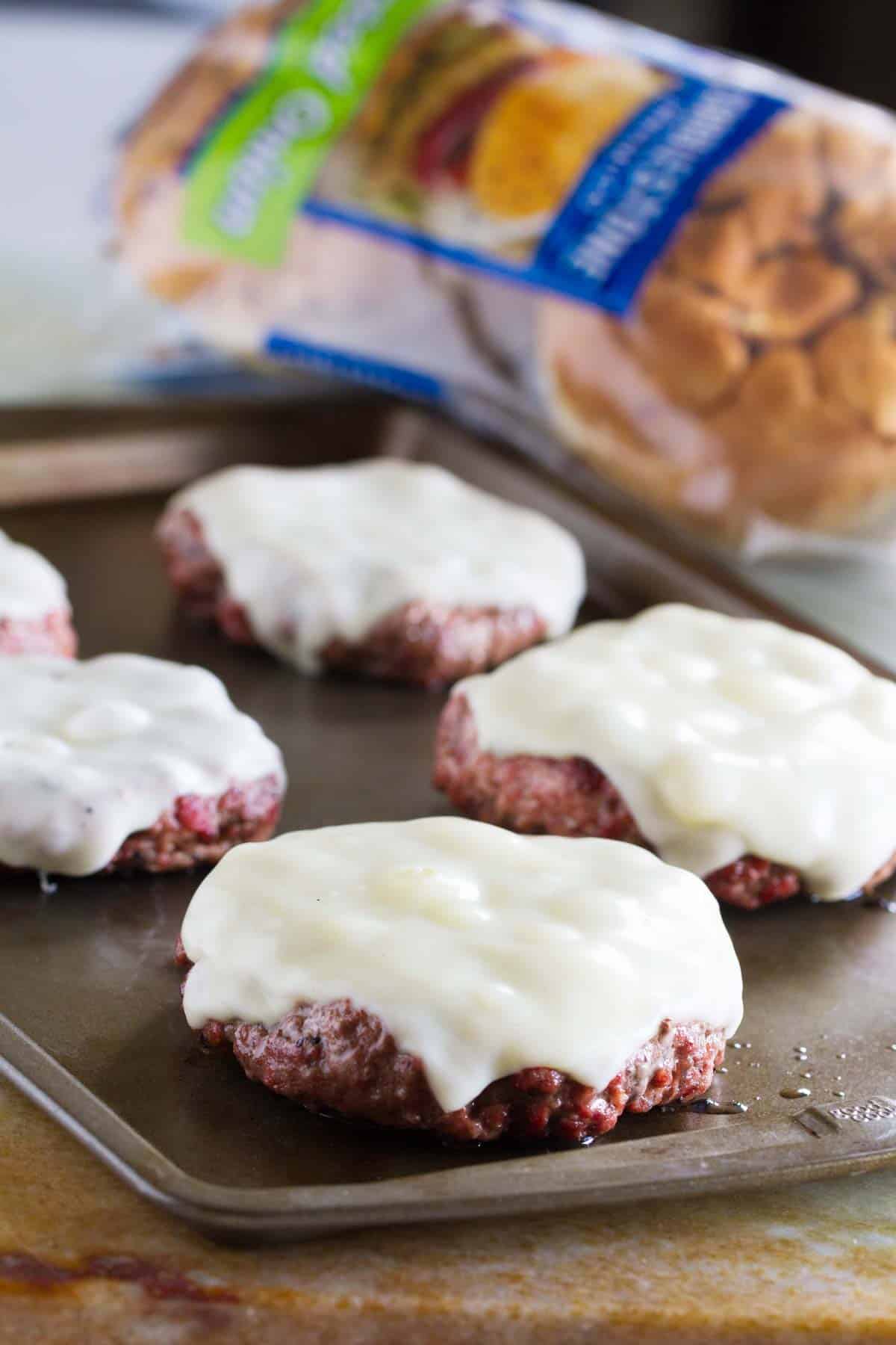 Burger patties with cheese on a baking sheet.