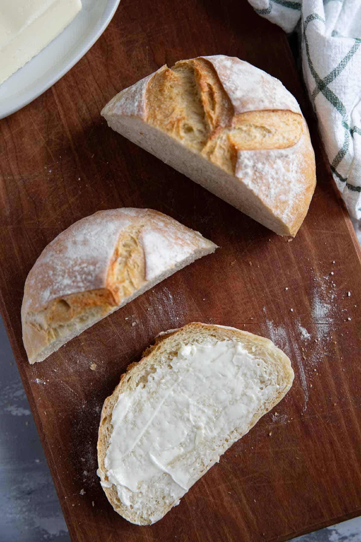 Loaf of artisan bread cut with butter spread on one slice.