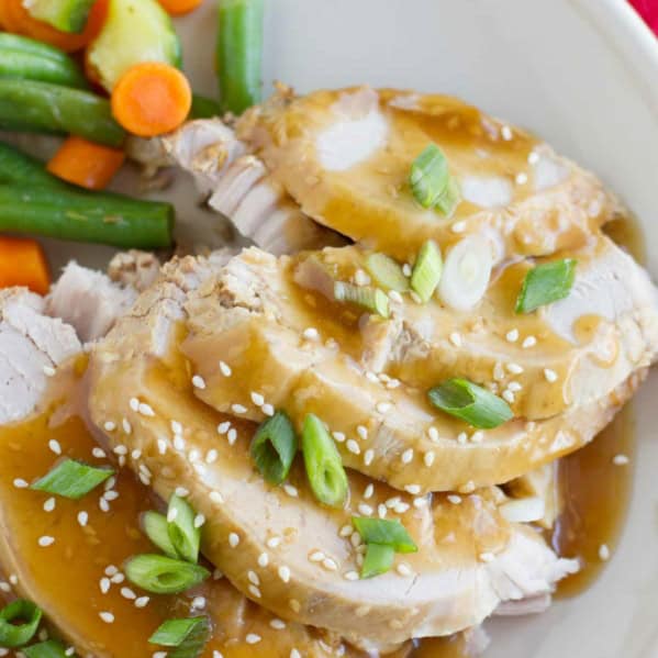 Slow Cooker Sesame Pork topped with sauce, green onions, and sesame seeds.