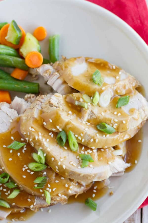 Slow Cooker Sesame Pork topped with sauce, green onions, and sesame seeds.