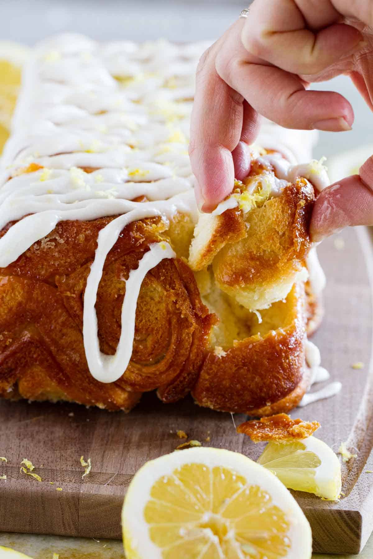 Fingers pulling a piece of lemon roll pull apart bread from the loaf.