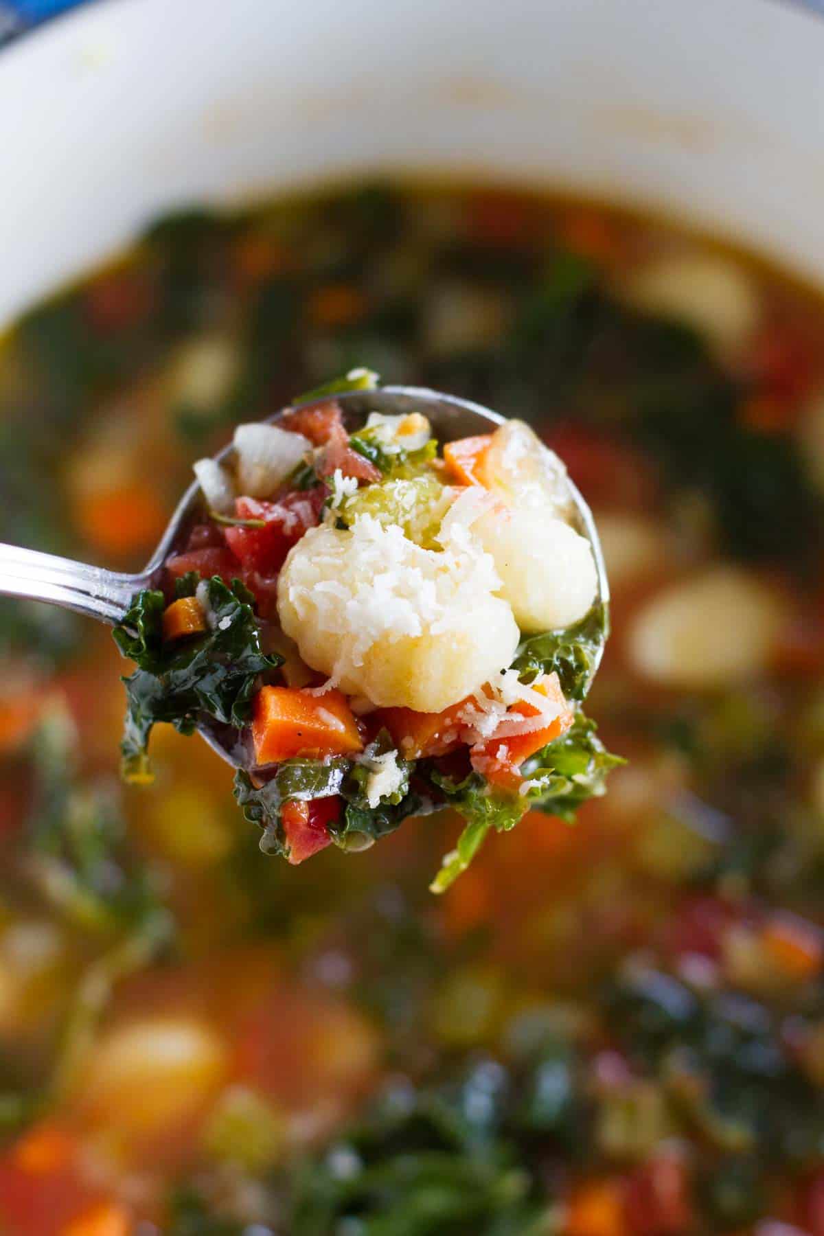 Ladle full of Minestrone with Gnocchi over a soup pot.