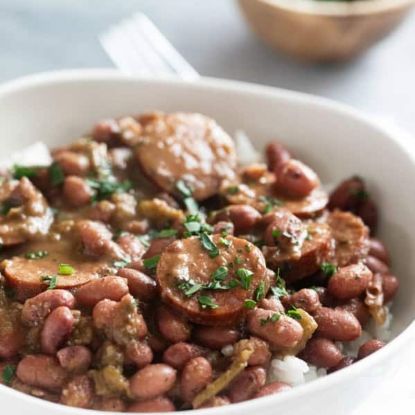 Bowl of rice topped with red beans and sausage, garnished with parsley.
