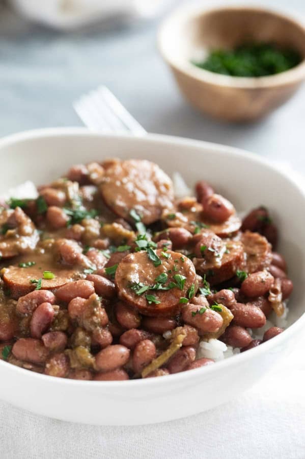 Bowl of rice topped with red beans and sausage, garnished with parsley.