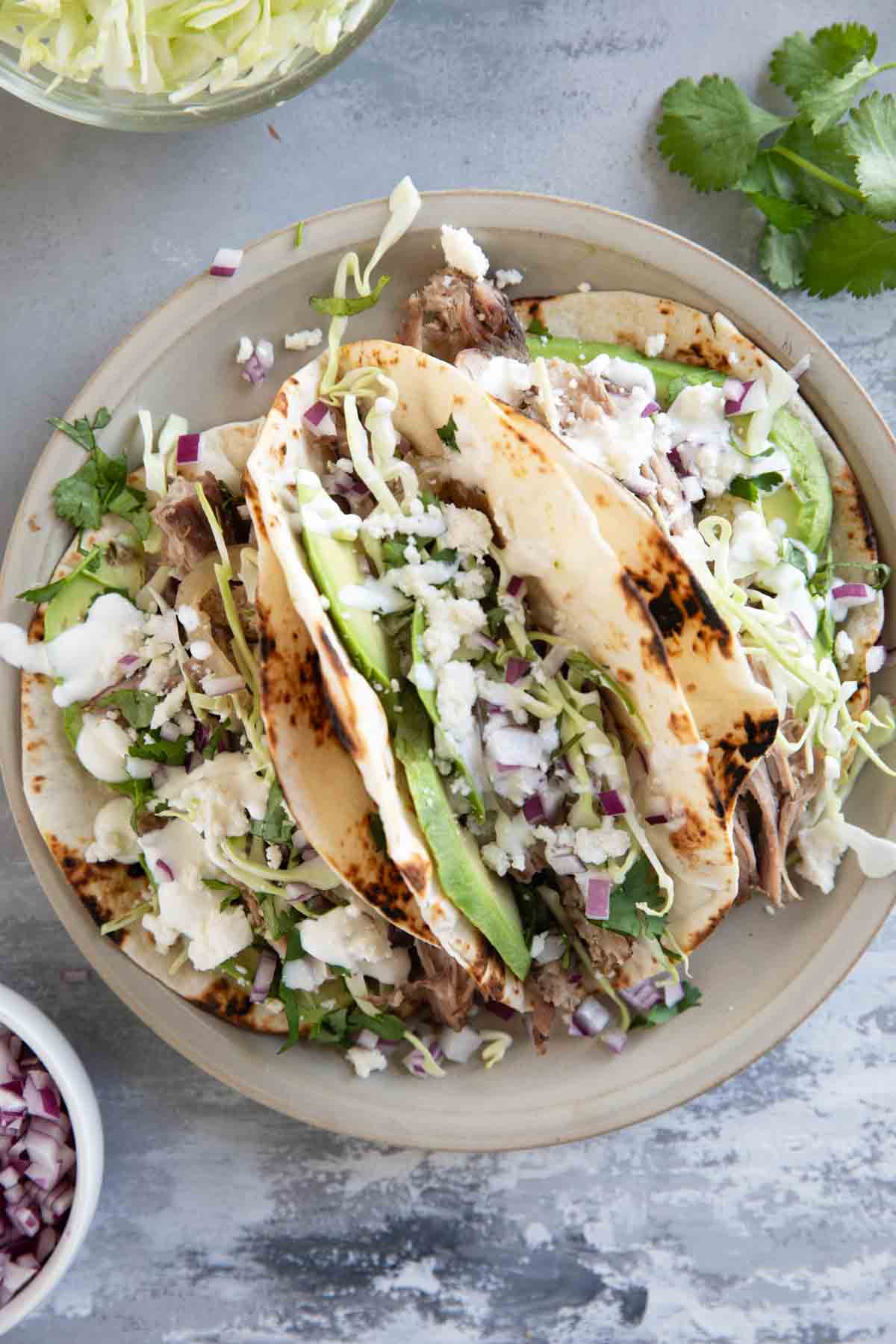 Three shredded pork tacos with charred tortillas on a plate.