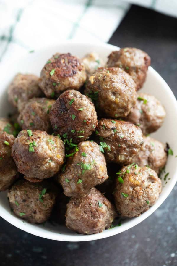 Baked meatballs in a bowl sprinkled with parsley.