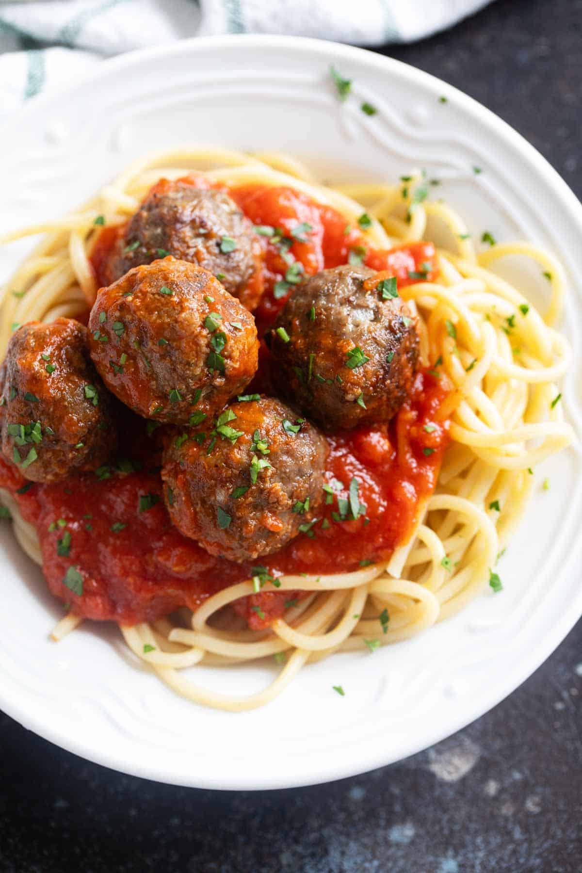 Baked meatballs with pasta sauce over spaghetti.