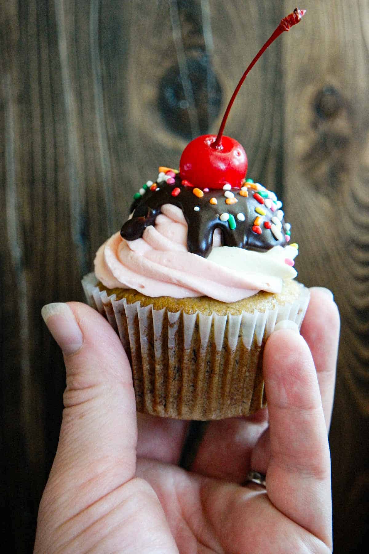 Hand holding a banana split cupcake.