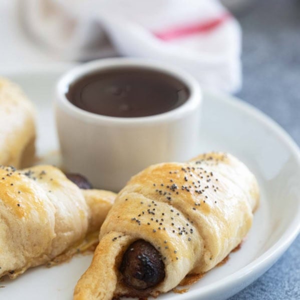 Breakfast Pigs in a Blanket on a plate with maple syrup for serving.