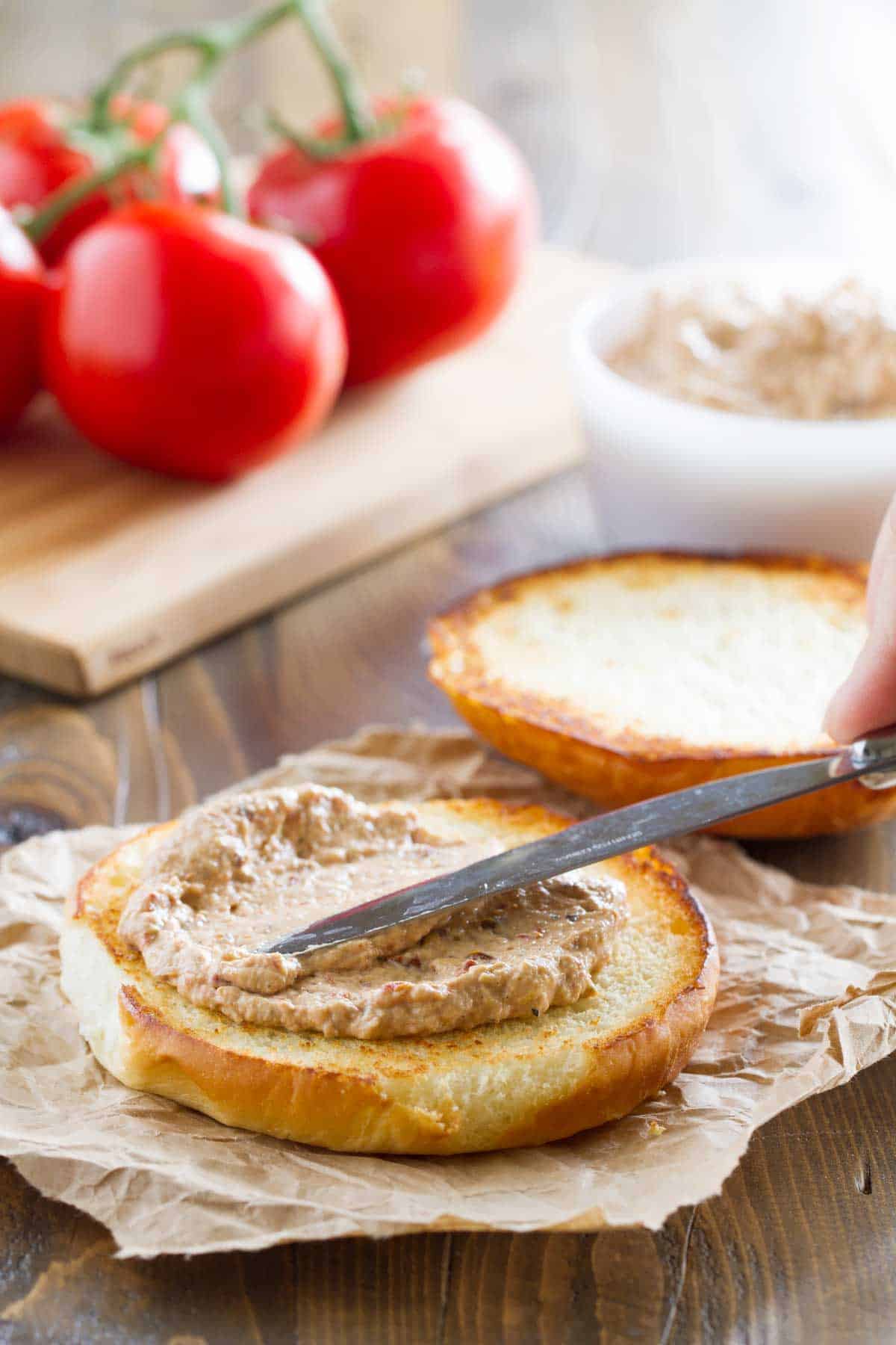 Spreading sun-dried tomato and artichoke spread on a burger bun.