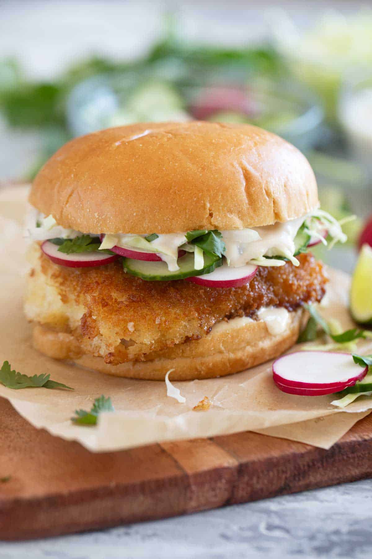Crispy Fish Sandwich topped with cucumber, radish, cabbage, and homemade wasabi tartar sauce.