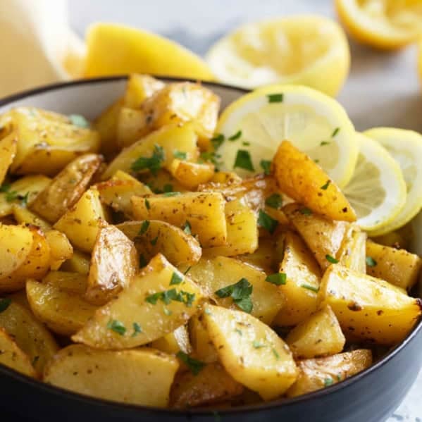 Bowl filled with roasted Greek Lemon Potatoes with lemon slices in the bowl.