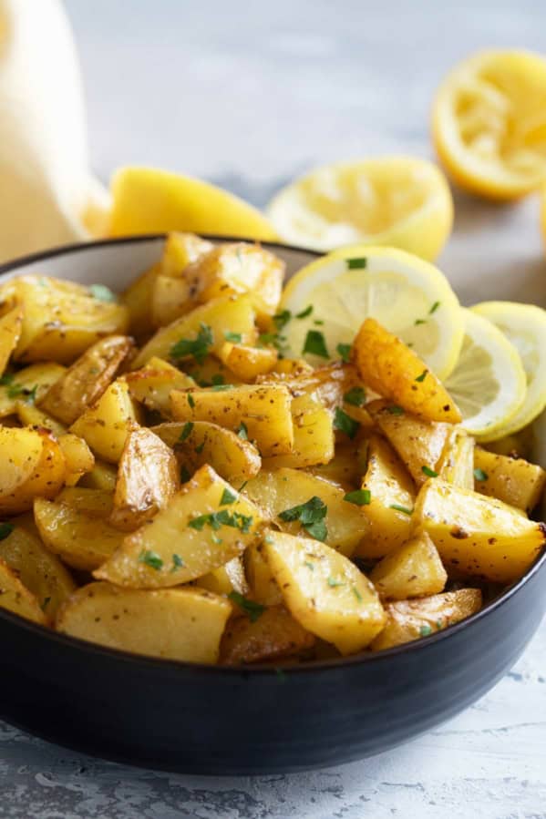 Bowl filled with roasted Greek Lemon Potatoes with lemon slices in the bowl.