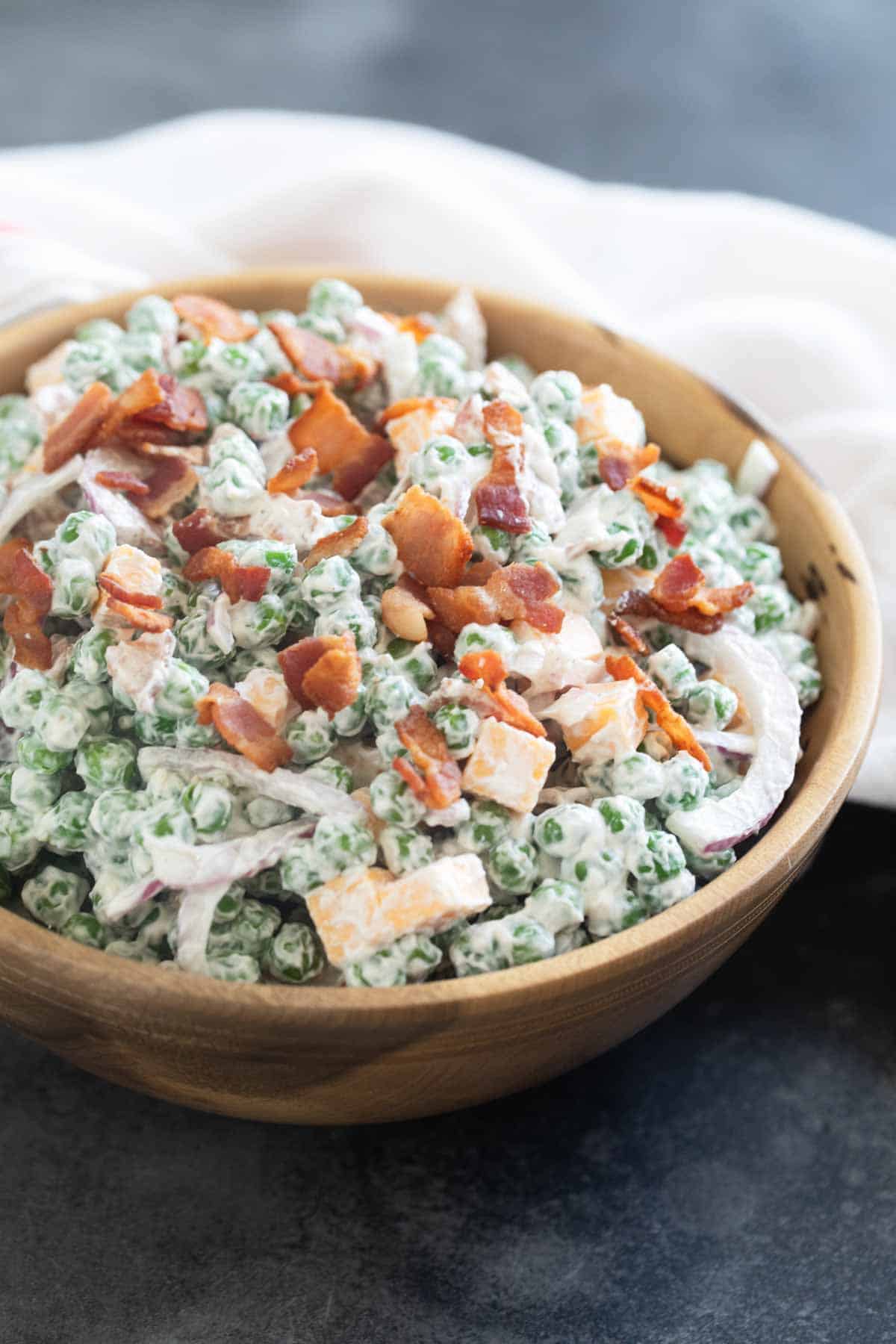 Pea Salad in a wooden bowl, topped with bacon.