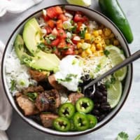 View of Pork Carnitas Burrito Bowl topped with jalapeños, pico de gallo, cheese, avocado, beans, sour cream, and more.