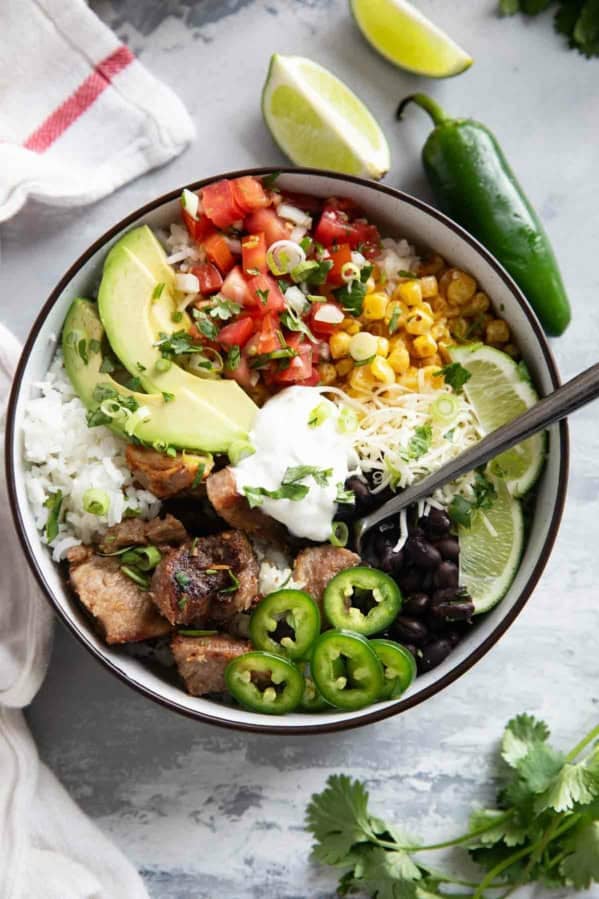 View of Pork Carnitas Burrito Bowl topped with jalapeños, pico de gallo, cheese, avocado, beans, sour cream, and more.