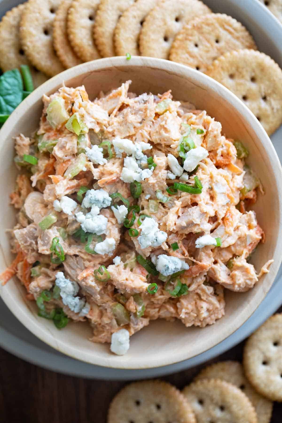 Wooden bowl filled with Buffalo Chicken Salad topped with crumbled blue cheese.