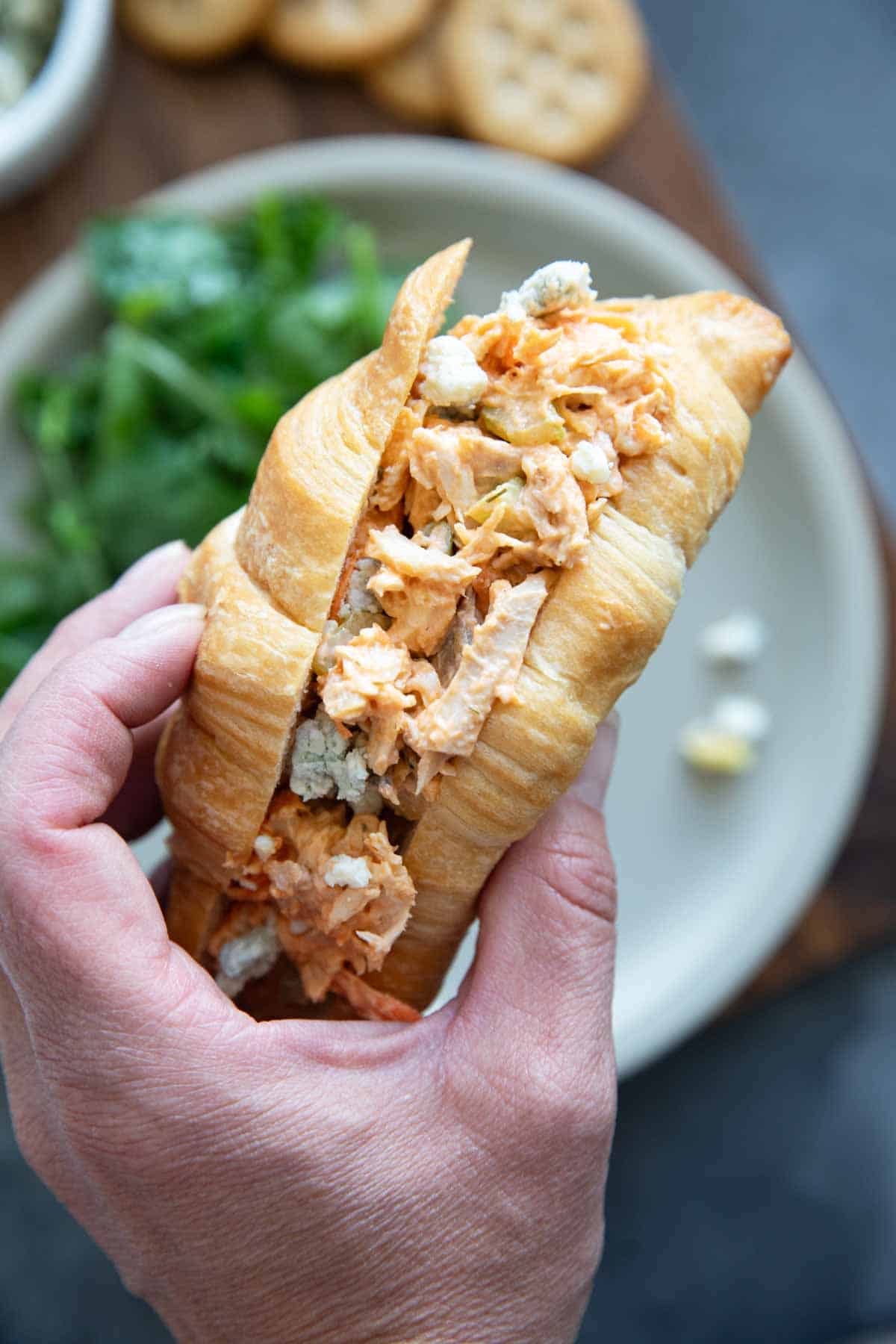 Hand holding buffalo chicken salad in a croissant.