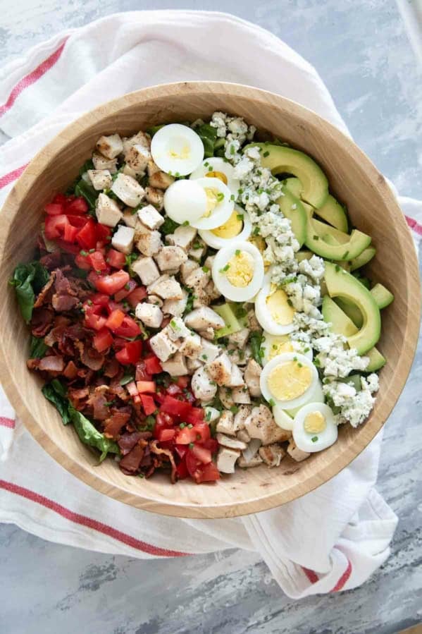 Cobb Salad with toppings arranged in lines on top in a large bowl.