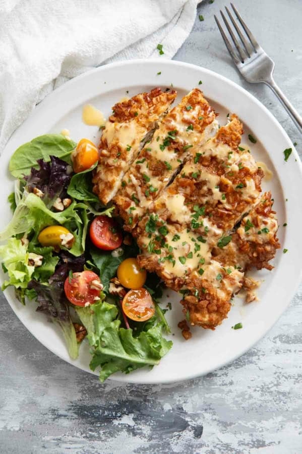 Pretzel Crusted Chicken with Mustard Cheddar Sauce with a side salad on a plate.