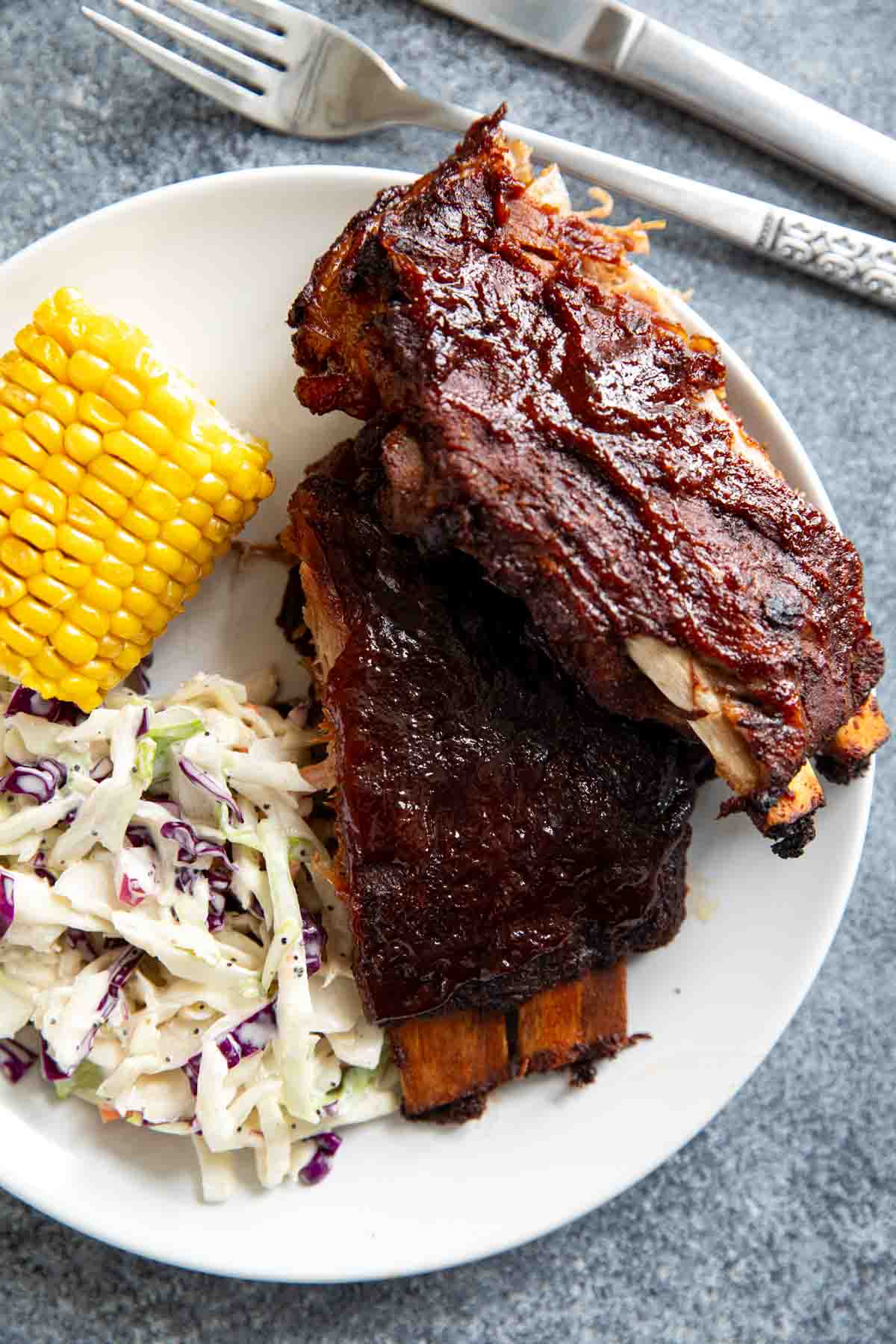 Slow Cooker Ribs on a plate with corn and coleslaw.