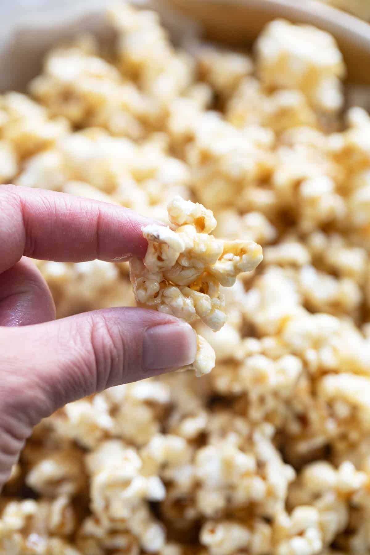 Fingers holding a piece of soft caramel popcorn.