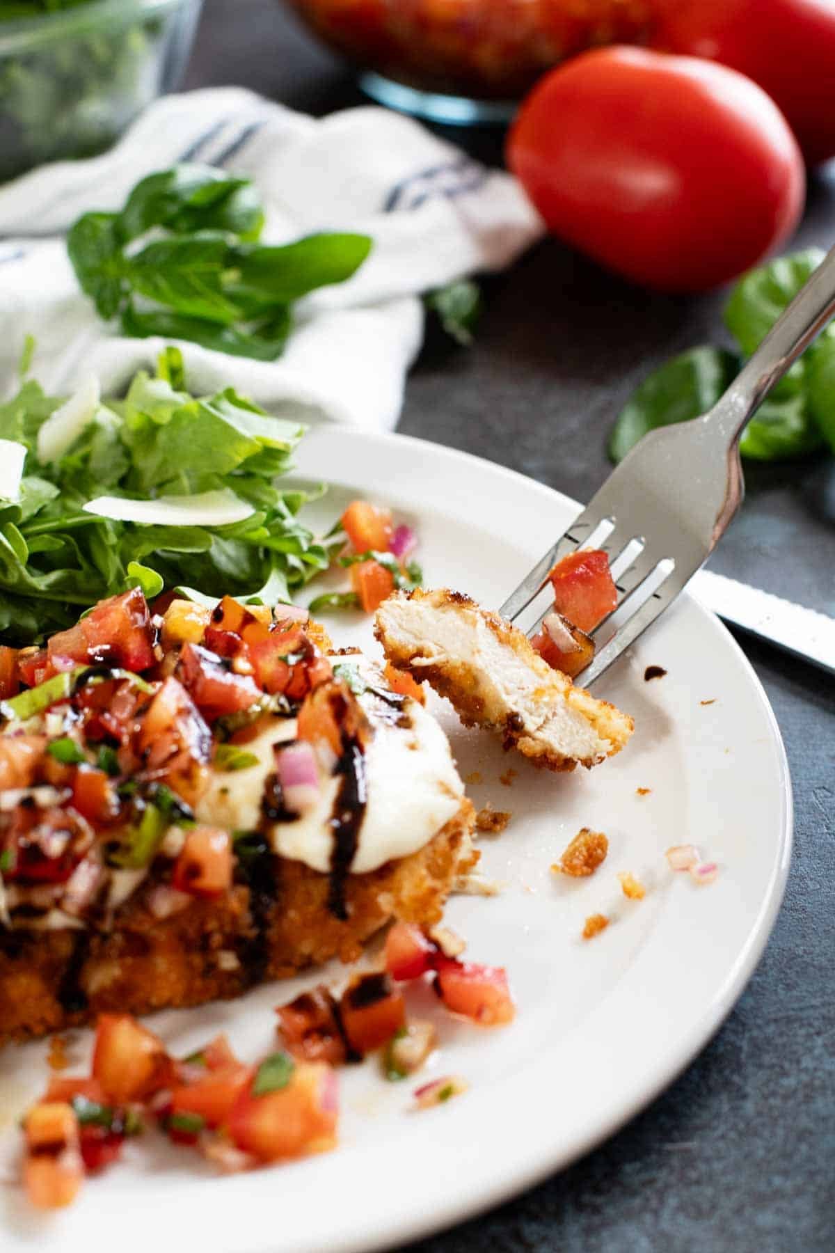 Bruschetta Chicken with a bite of the chicken on a fork.