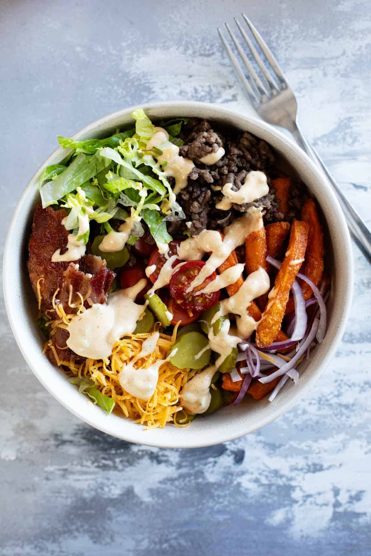 Burger Bowls with beef, sweet potato fries, onions, tomatoes, cheese, bacon, and more.