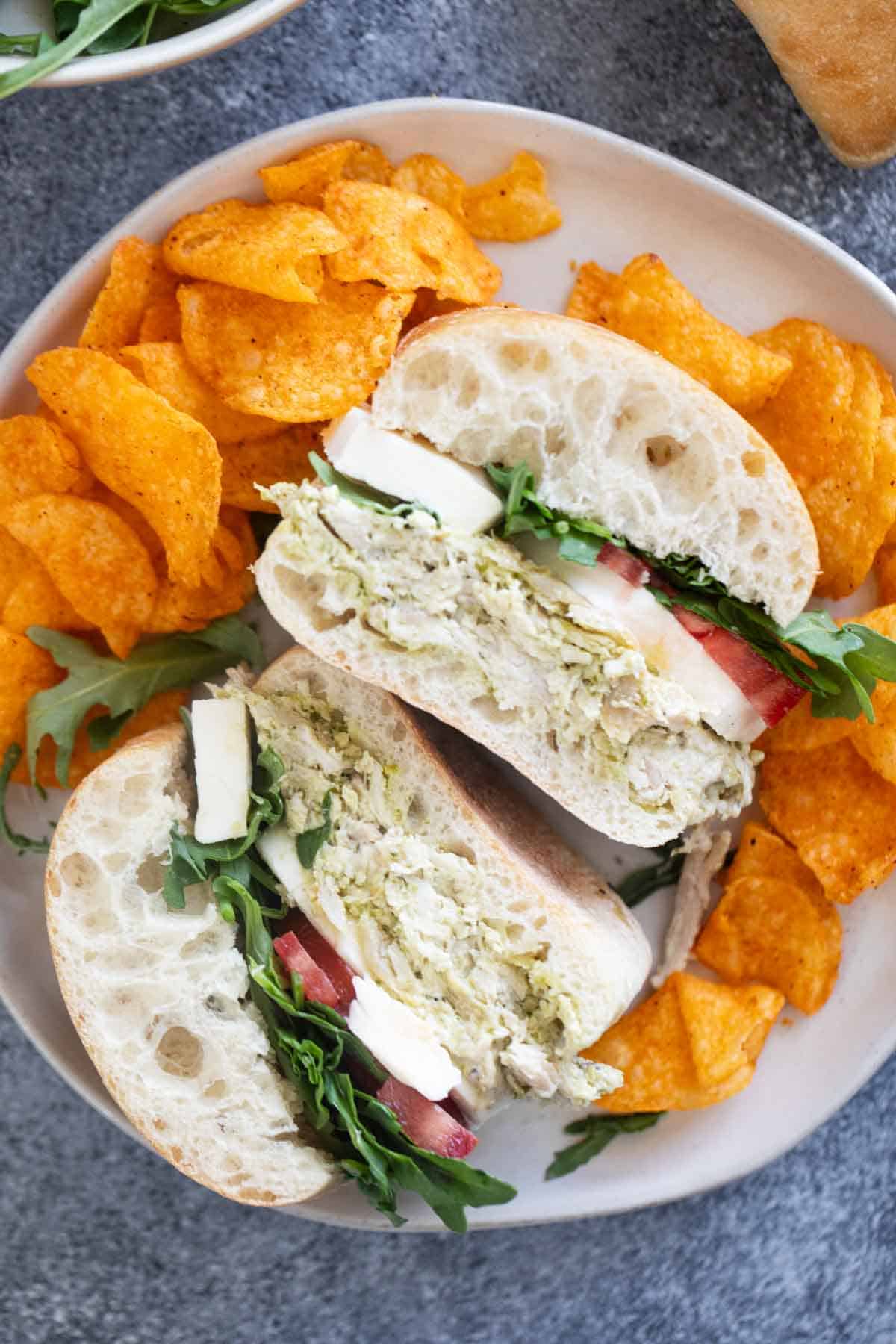 Chicken Pesto Sandwich cut in half on a plate with potato chips.